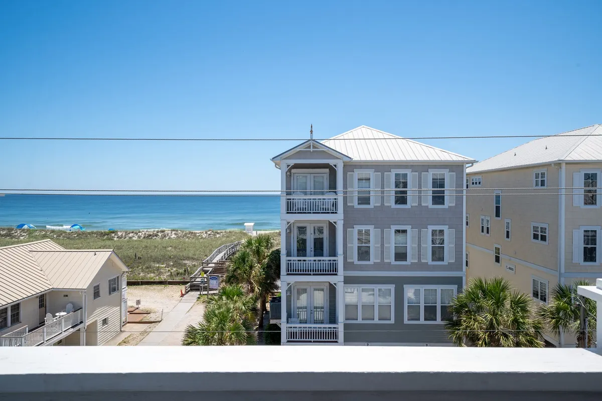 A stunning view of a beachfront property with lush palm trees, expansive ocean views, and balconies that capture the sunset. The scene invites beach lounging, swimming, and family gatherings, with the shoreline just steps away.