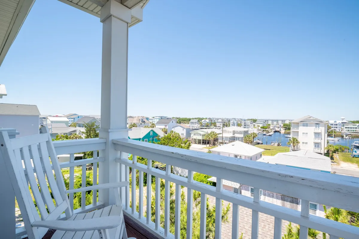 A cozy balcony with a rocking chair overlooking the water, bordered by a classic railing. The tranquil waterfront view invites relaxation and offers a sense of place—ideal for unwinding after a day of activities or enjoying gentle coastal breezes.