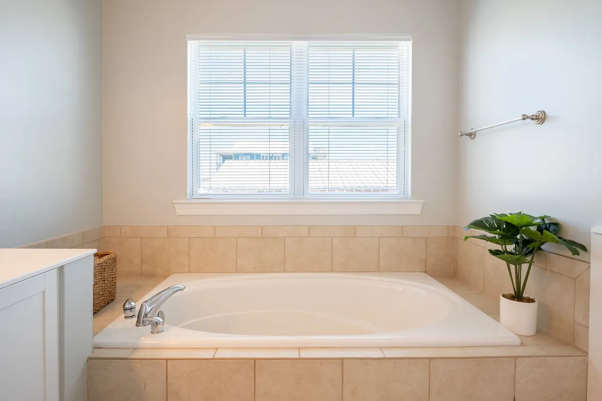 A tranquil en suite bathroom with a deep soaking tub set next to a window, accentuated by a touch of greenery. Natural light fills the space, highlighting the calming environment ideal for relaxation at the end of the day.