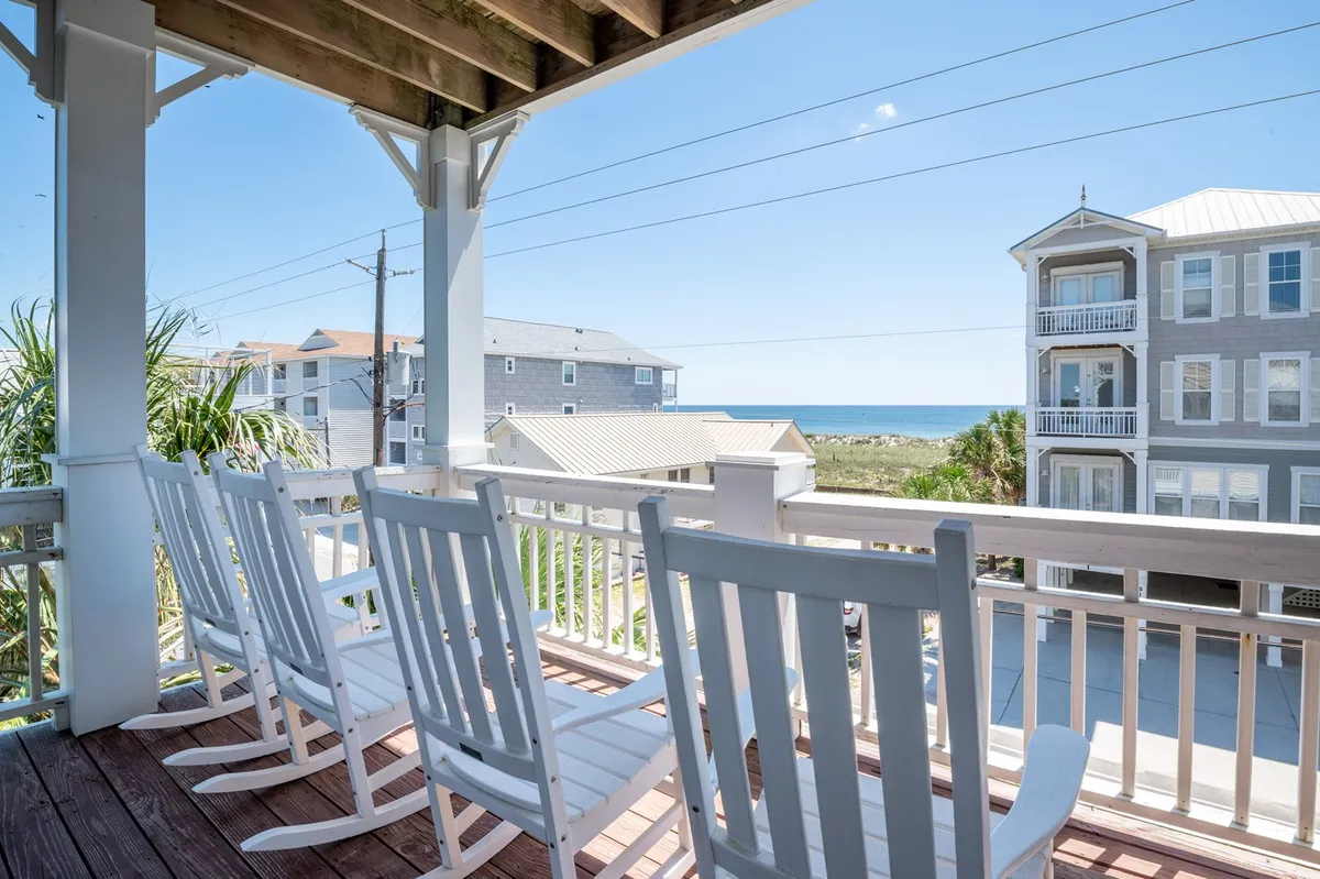 A cozy balcony with classic rocking chairs faces the ocean, framed by a sturdy railing. The view stretches toward the horizon, promising both sunrise and sunset vistas and a tranquil spot for relaxation or stargazing.