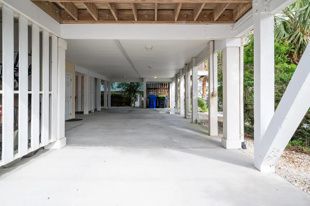 A functional parking area featuring visible support beams, a concrete floor, and exterior doors. The space includes organized garbage bins, suggesting a well-maintained and practical area for vehicle storage and access after a day out.