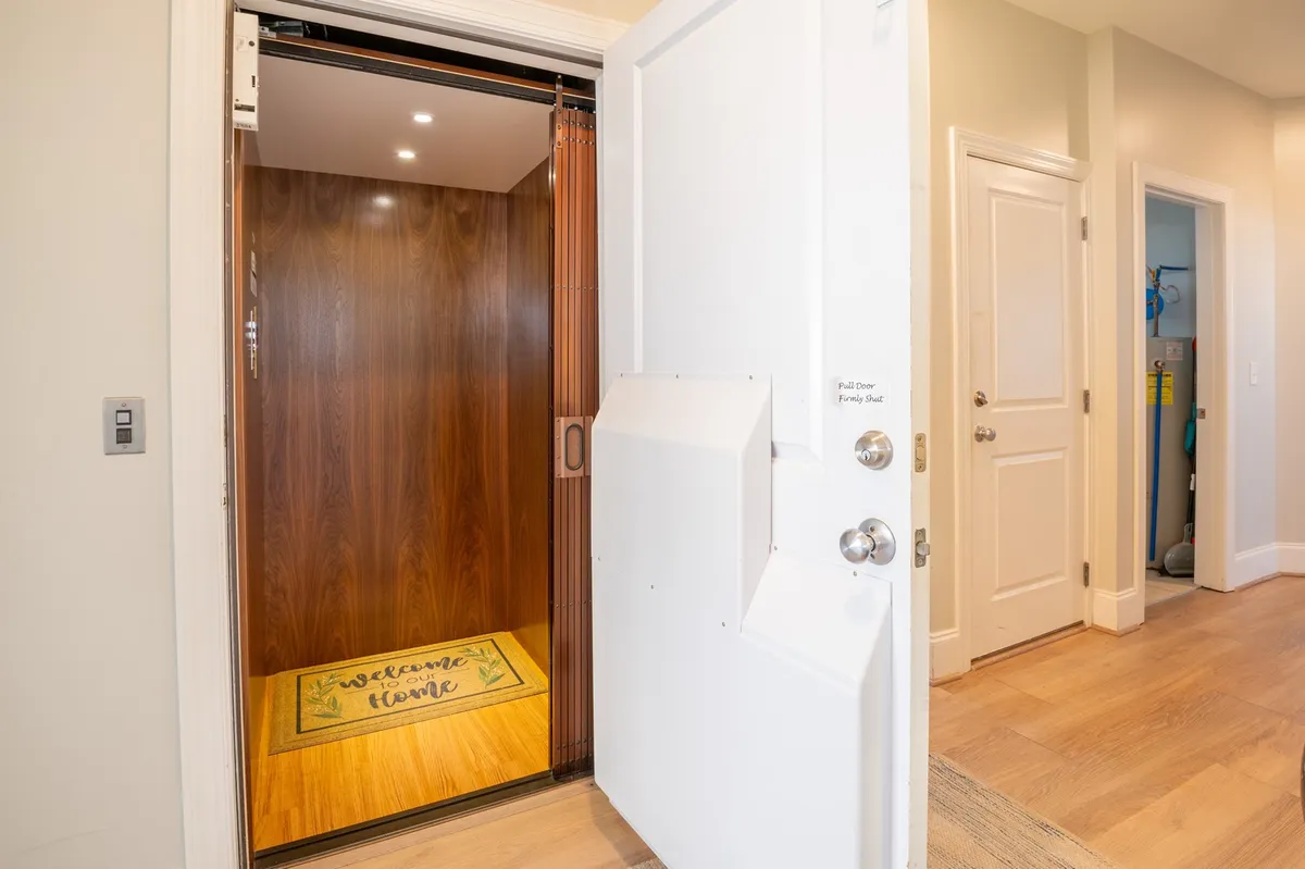 A small elevator sits beside a welcome mat, its door open to reveal the practical convenience it offers to guests. The setting provides a glimpse of the entryway, highlighting how the elevator helps with ease of access for luggage and groceries.