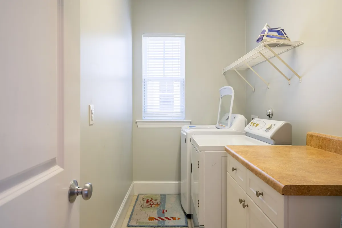 A bright laundry room with a washing machine, dryer, ample countertop space, and a window letting in natural light. The clean and organized space invites guests to handle laundry needs efficiently during their stay.